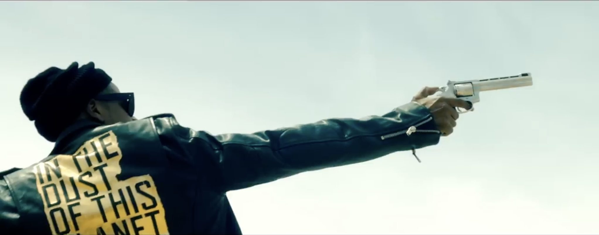 Jay-Z photographed from the back holding a revolver. The text "In the Dust of This Planet" can be seen on his back.